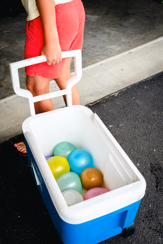 A child pulls a cooler filled with colorful water balloons.